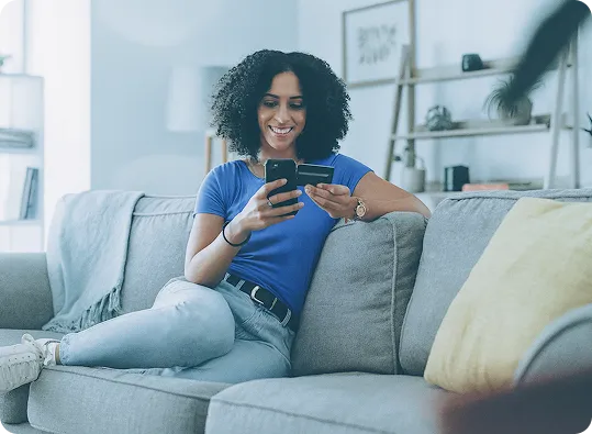 A cheerful customer shops from an OrderEazi store from the comfort of her sofa, smartphone and credit card in hand.