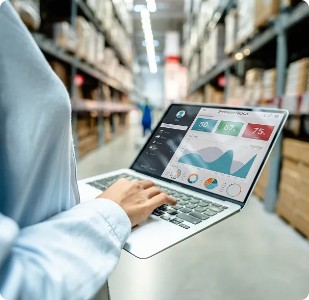 A warehouse worker uses OrderEazi's analytics dashboard on a laptop amidst towering inventory shelves.