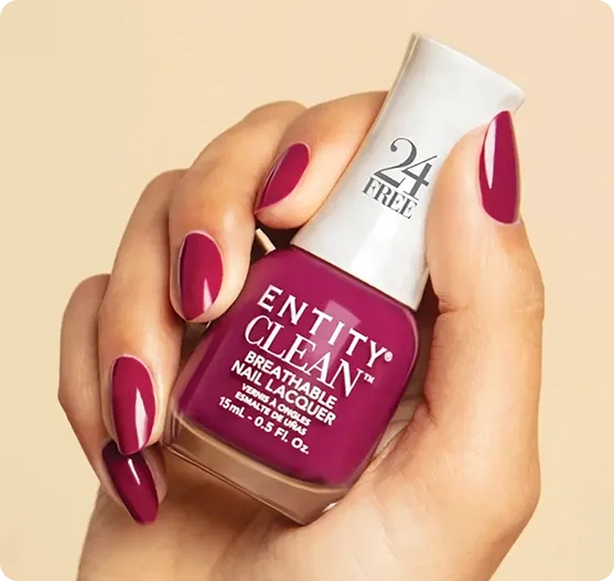 A hand with burgundy-colored manicured nails holds a bottle of Entity Clean nail polish in the same deep burgundy shade.
