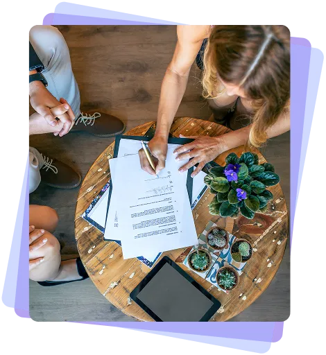 Overhead view of two people collaborating at a wooden table. 
