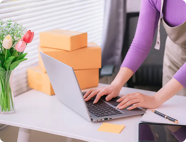 A person in a purple jumper types on a silver laptop, positioned on a white desk. 